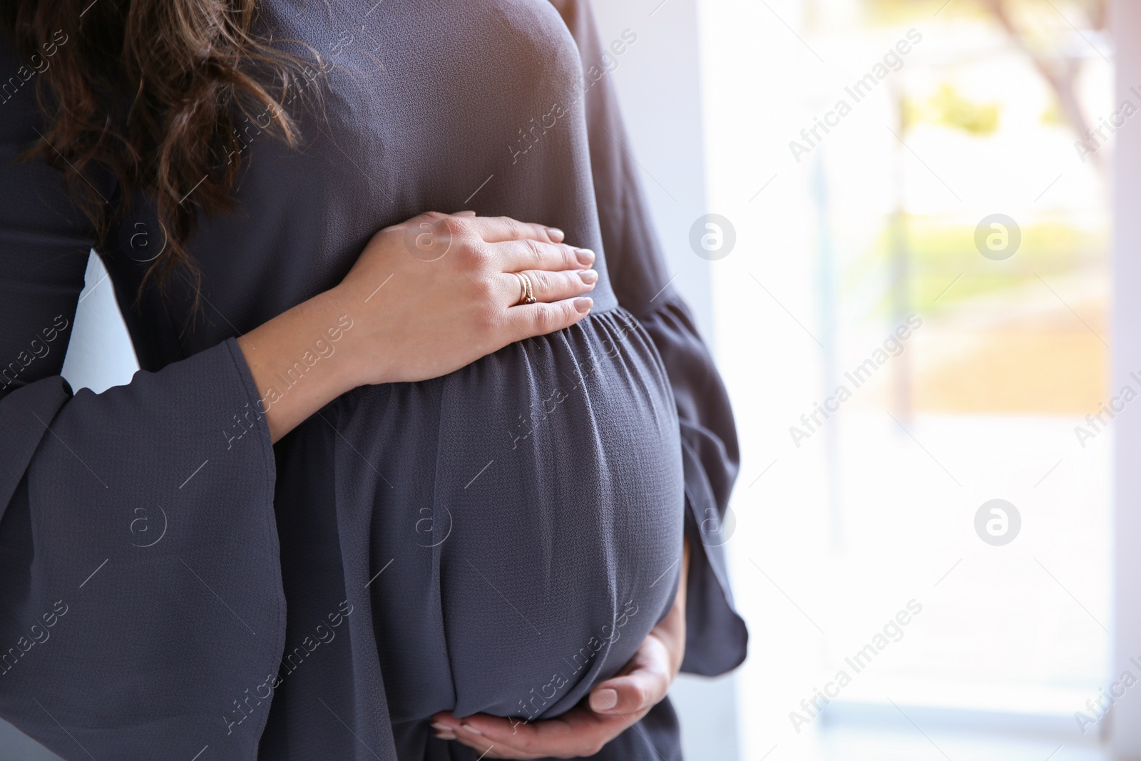 Photo of Young pregnant woman near window at home, closeup. Space for text