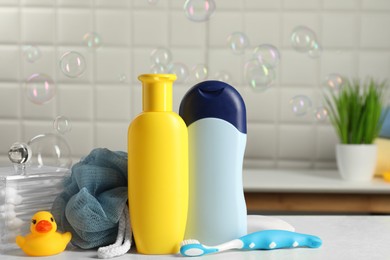 Photo of Baby cosmetic products, bath duck, toothbrush and sponge on white table against soap bubbles. Space for text