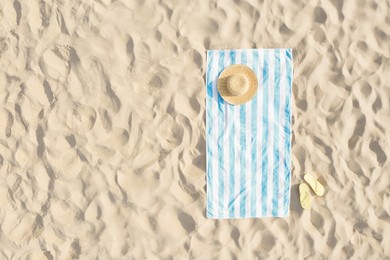 Image of Striped beach towel, straw hat and flip flops on sand, aerial view. Space for text
