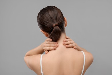 Woman touching her neck on grey background, back view