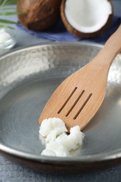 Photo of Frying pan with organic coconut cooking oil and wooden spatula on grey table, closeup