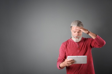 Portrait of handsome mature man with tablet on color background