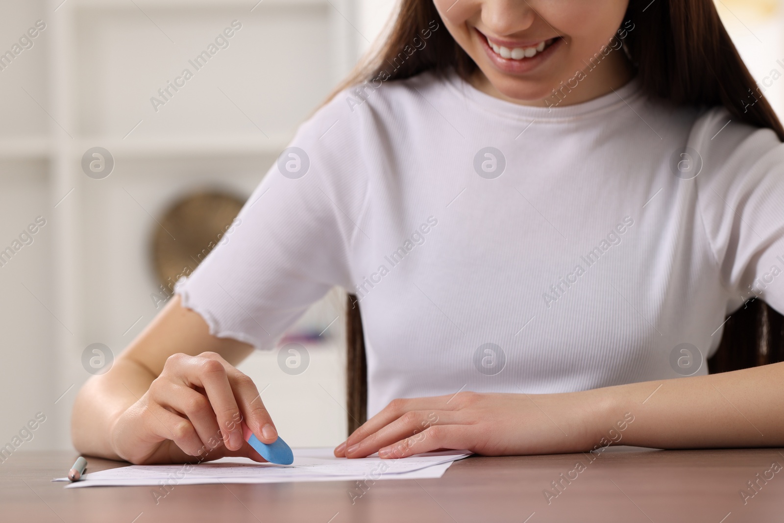 Photo of Teenage girl erasing mistake in her notebook at wooden desk indoors, closeup