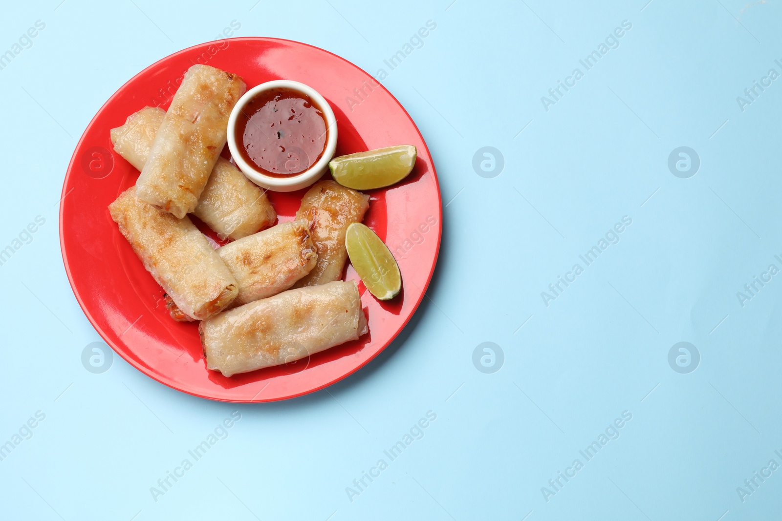 Photo of Tasty fried spring rolls, lime and sauce on light blue table, top view. Space for text