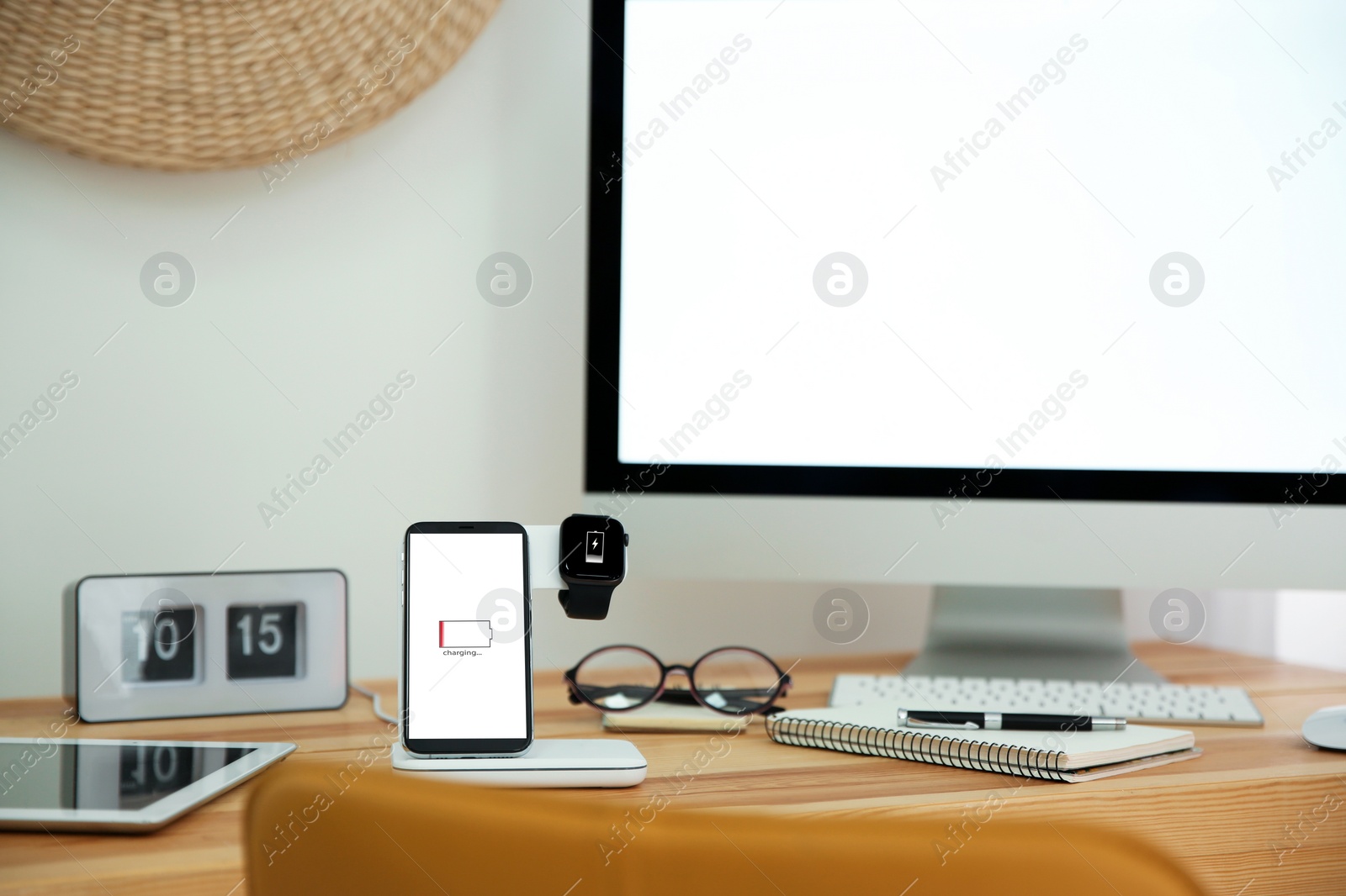 Photo of Mobile phone and smartwatch with wireless charger on wooden table. Modern workplace accessory