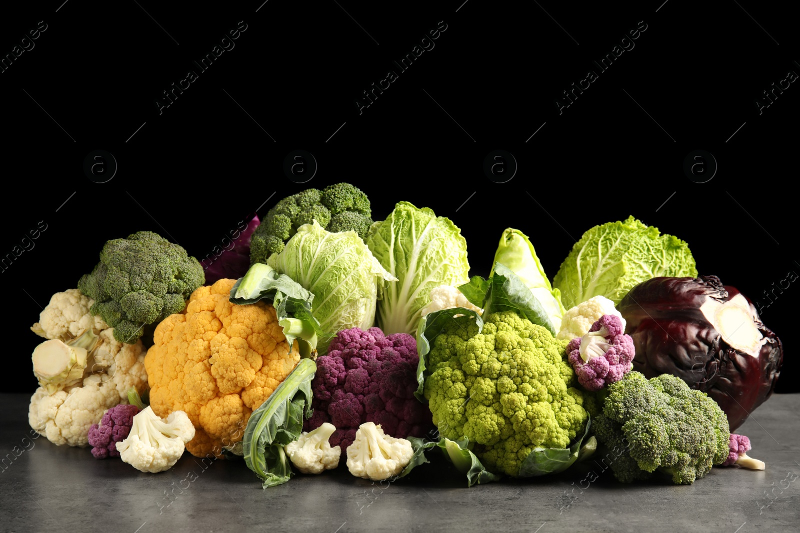 Photo of Different fresh cabbages on table against black background. Healthy food