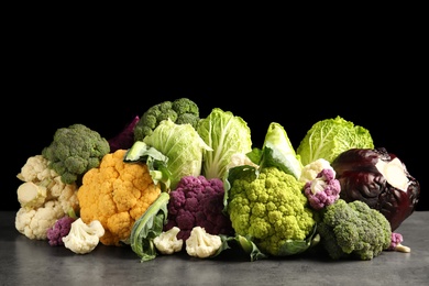 Photo of Different fresh cabbages on table against black background. Healthy food