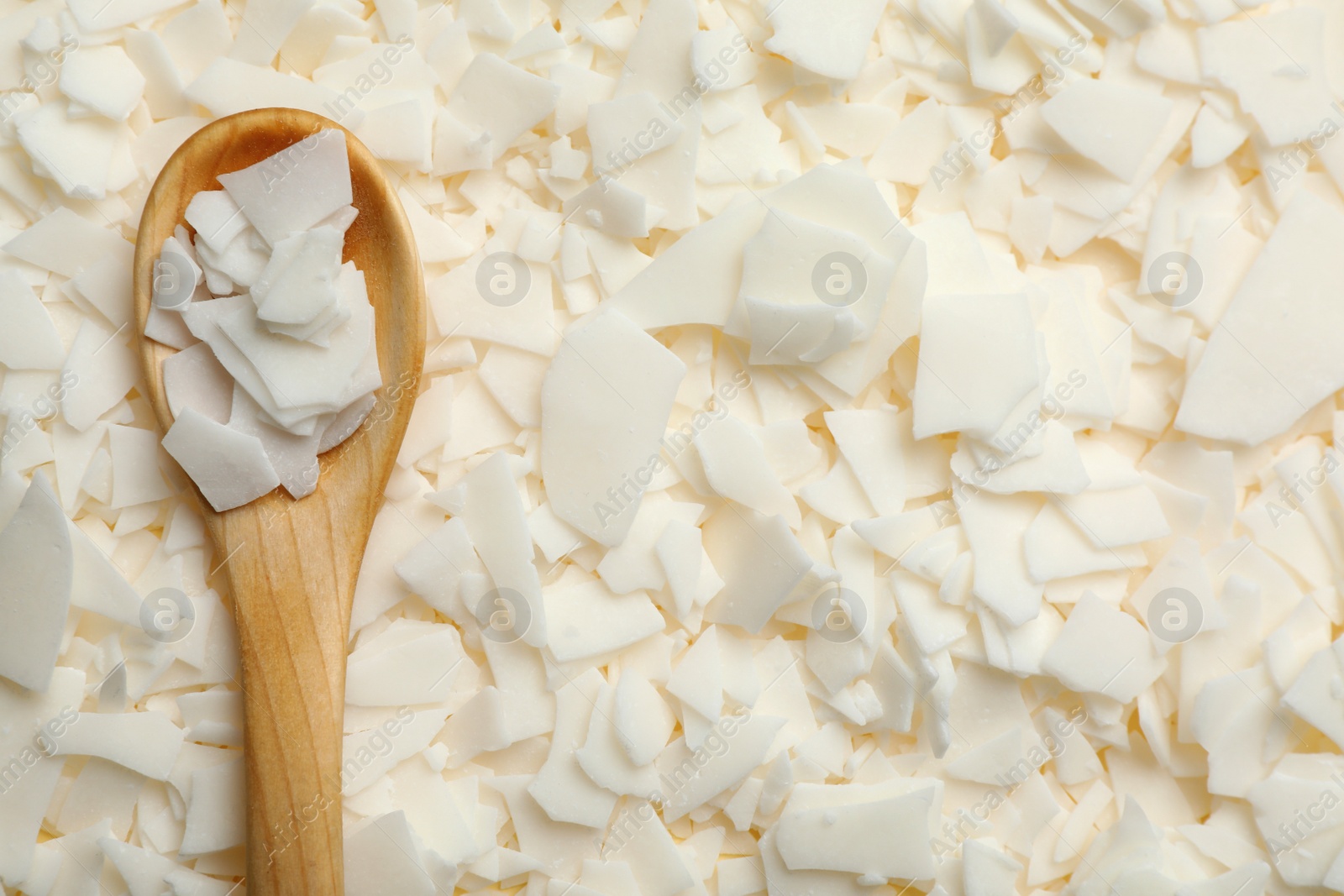 Photo of Wooden spoon on heap of soy wax flakes, top view. Homemade candle material