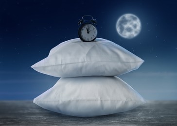 Image of Soft pillows and alarm clock on grey table against night sky with full moon. Insomnia