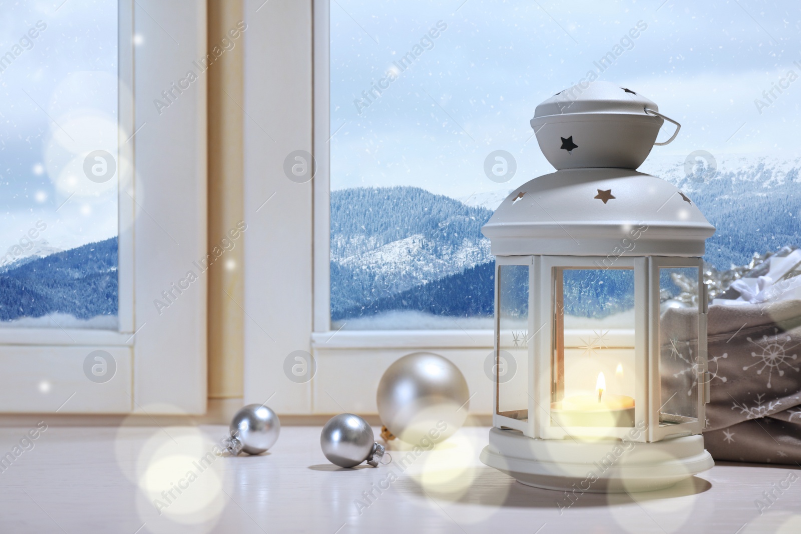 Image of White Christmas lantern with burning candle and festive decor on window sill indoors 