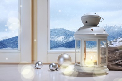 White Christmas lantern with burning candle and festive decor on window sill indoors 