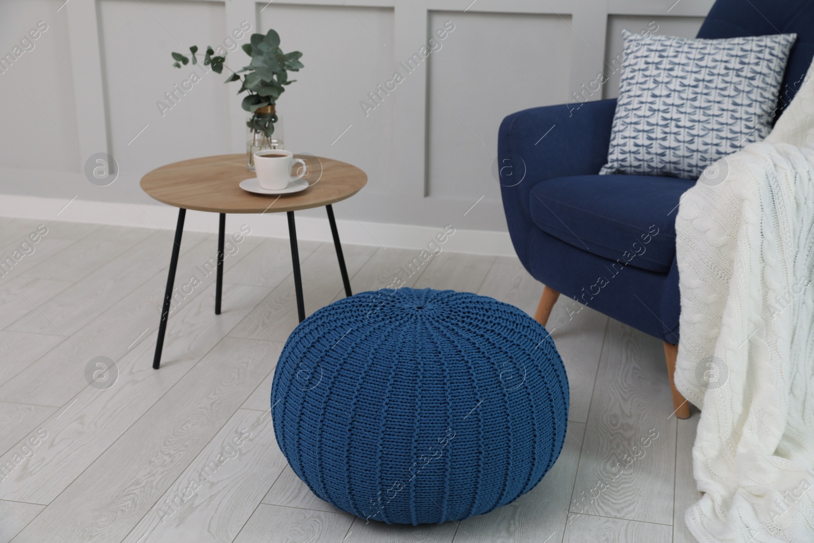 Photo of Stylish blue pouf near armchair in room. Interior design