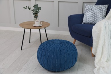 Stylish blue pouf near armchair in room. Interior design