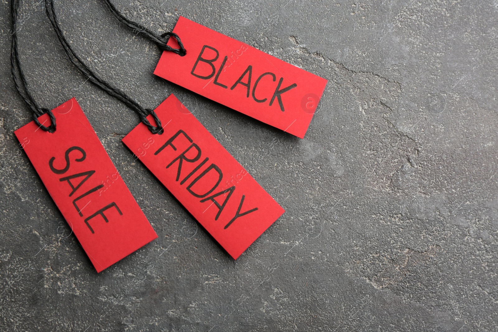 Photo of Red tags with words BLACK FRIDAY SALE on grey stone background, flat lay. Space for text