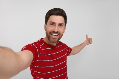Photo of Smiling man taking selfie and showing thumbs up on white background