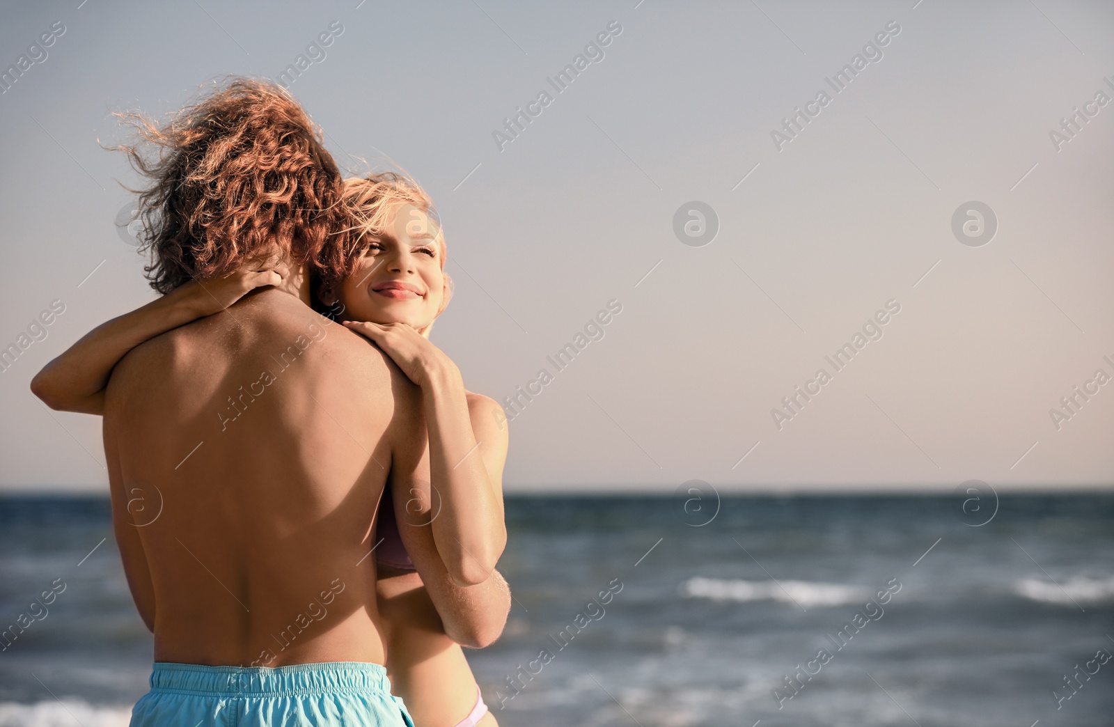 Photo of Young woman in bikini and her boyfriend on beach at sunset. Lovely couple