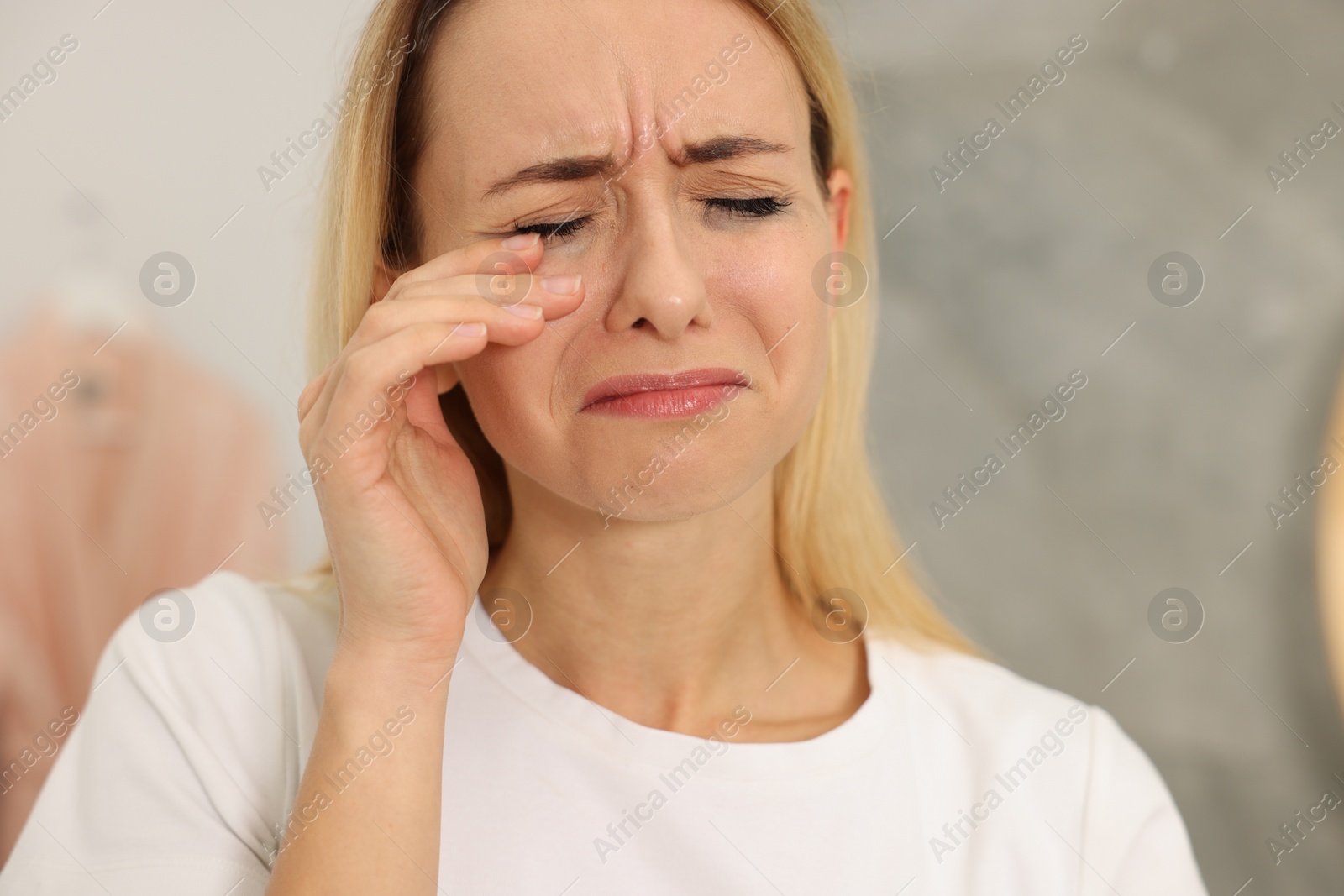 Photo of Sad woman with smeared mascara crying indoors, closeup