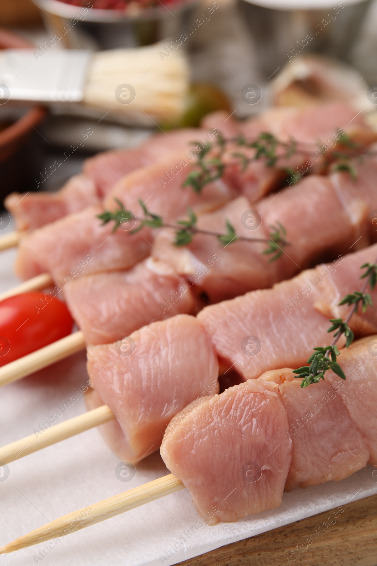 Photo of Skewers with cut raw meat and thyme on wooden board, closeup