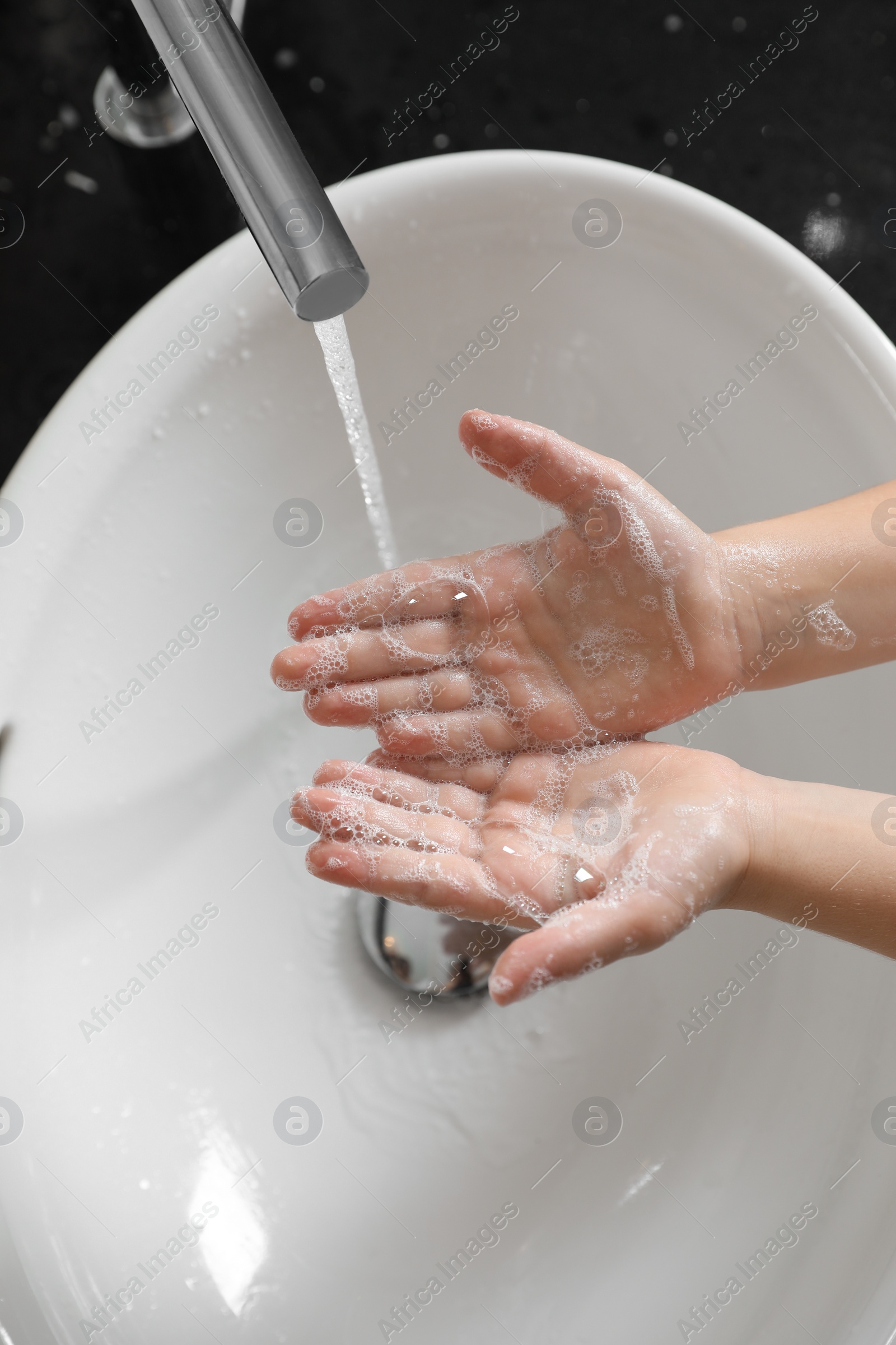 Photo of Little boy washing hands with soap over sink in bathroom, above view