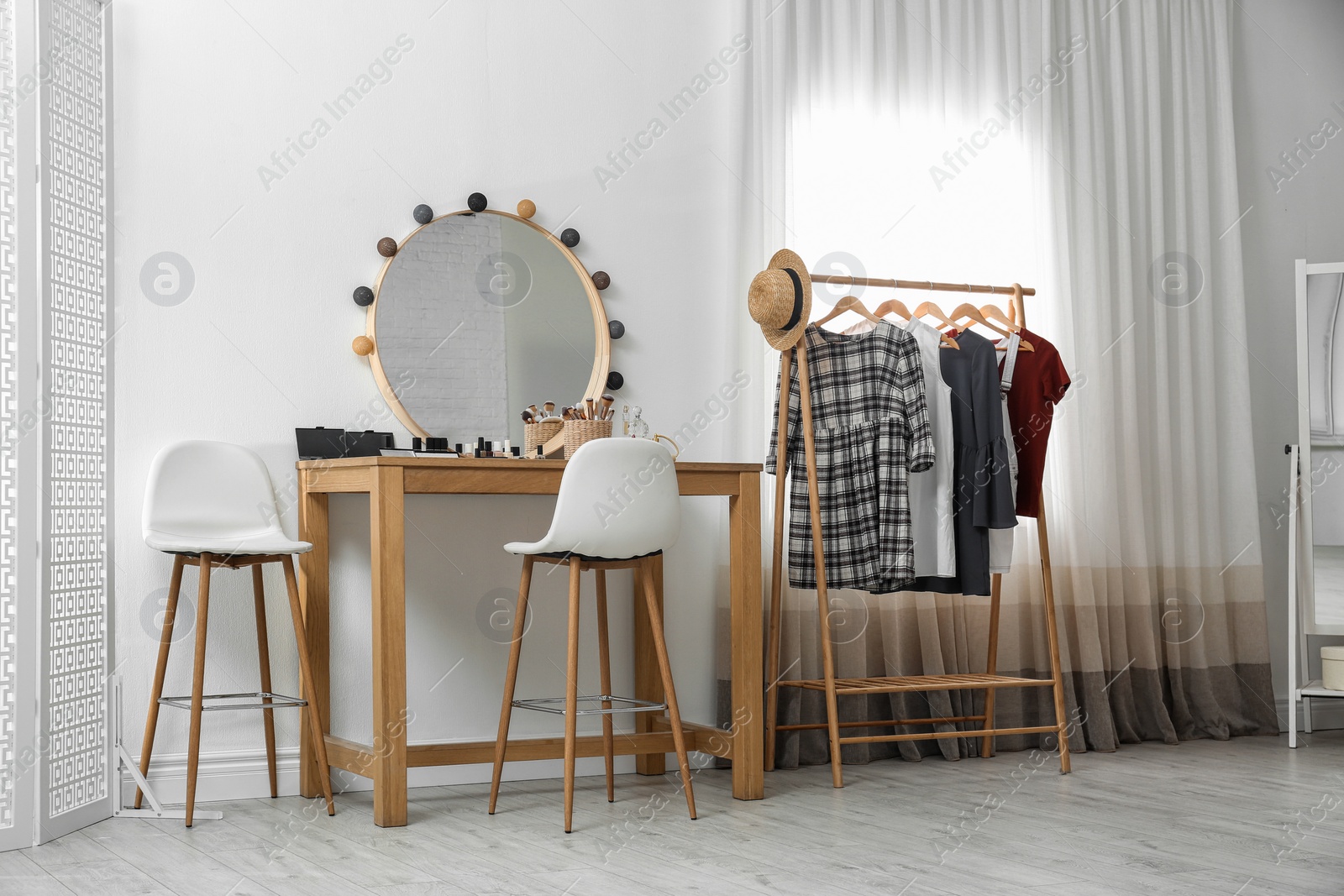 Photo of Hangers with stylish clothes on rack and dressing table in makeup room