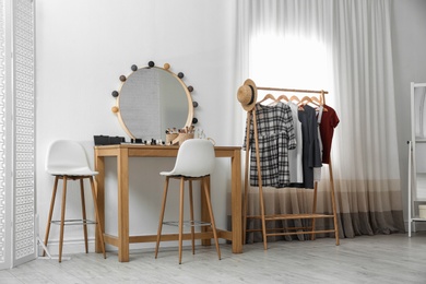 Photo of Hangers with stylish clothes on rack and dressing table in makeup room