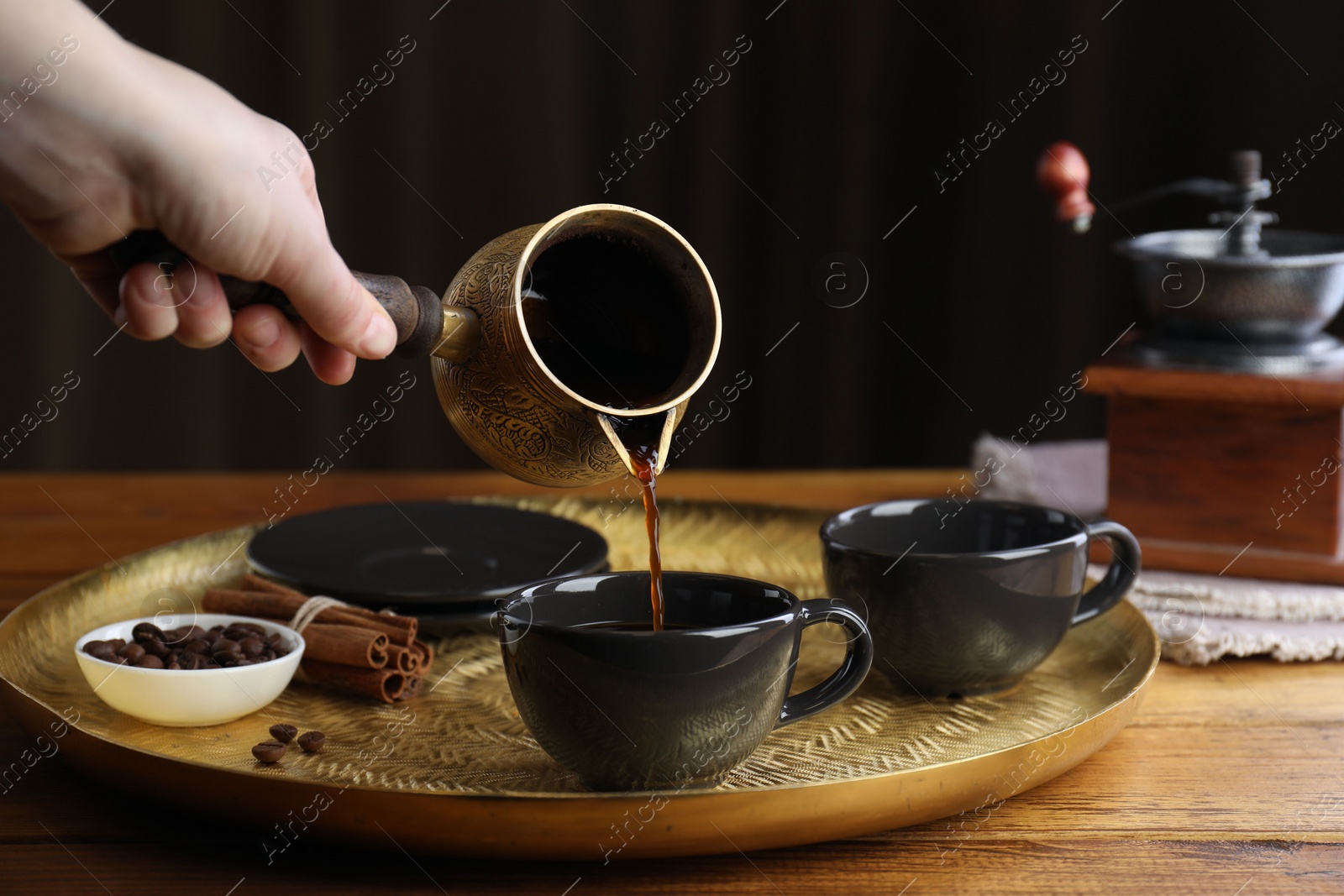 Photo of Turkish coffee. Woman pouring brewed beverage from cezve into cup at wooden table, closeup