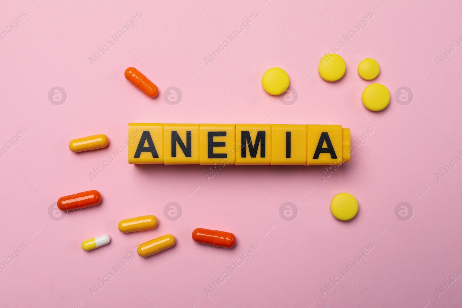 Photo of Word Anemia made with yellow cubes and pills on pink background, flat lay