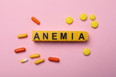 Photo of Word Anemia made with yellow cubes and pills on pink background, flat lay