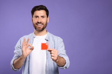 Photo of Man with condom showing ok gesture on purple background, space for text. Safe sex