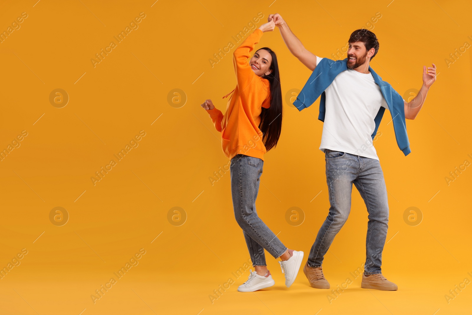 Photo of Happy couple dancing together on orange background, space for text