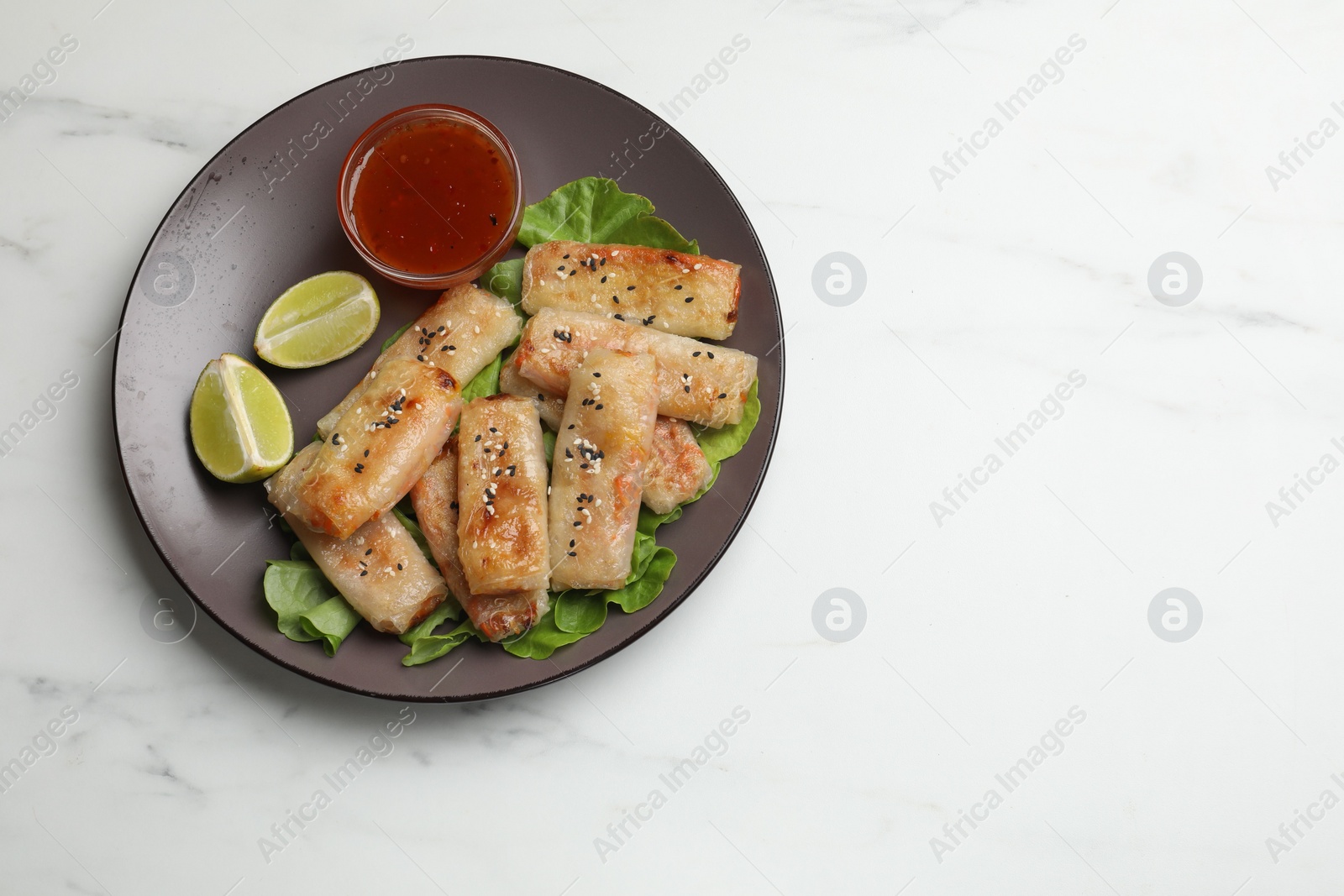 Photo of Tasty fried spring rolls and sauce on white marble table, top view. Space for text