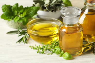 Photo of Different fresh herbs with oils on white wooden table, closeup