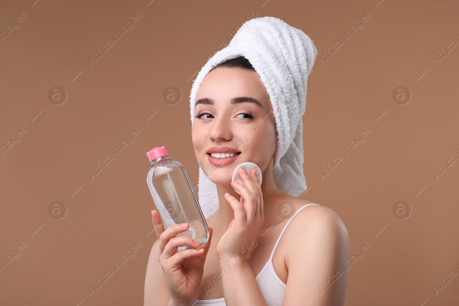 Photo of Beautiful woman in terry towel removing makeup with cotton pad on beige background