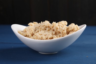 Photo of Bowl of tasty prepared horseradish on blue wooden table, closeup