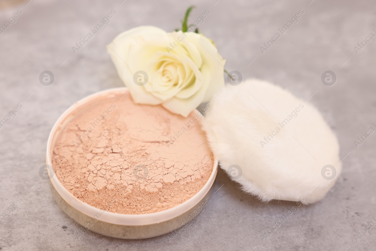 Photo of Face powder, puff applicator and rose flower on grey textured table, closeup