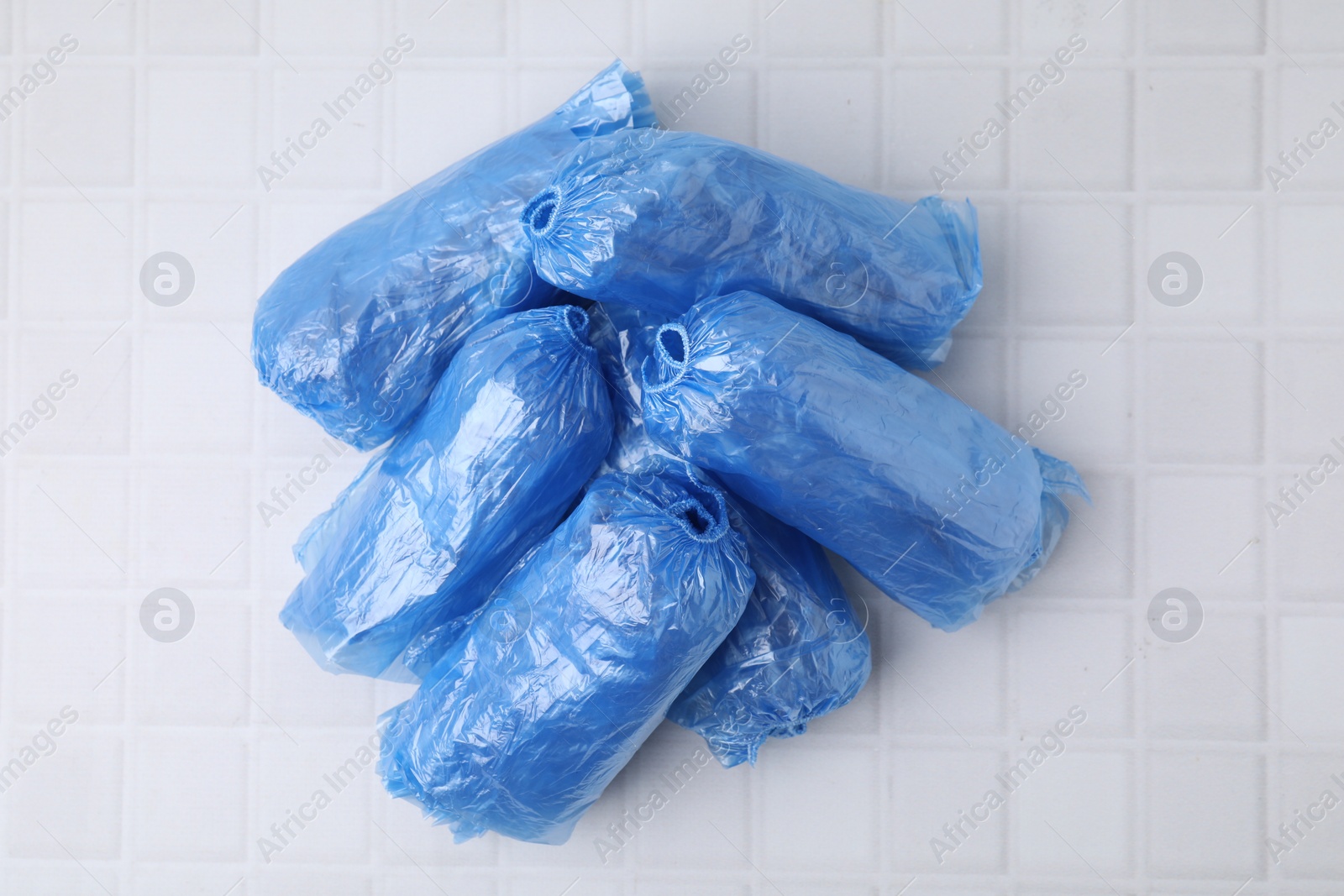 Photo of Rolled blue shoe covers on white tiled table, top view