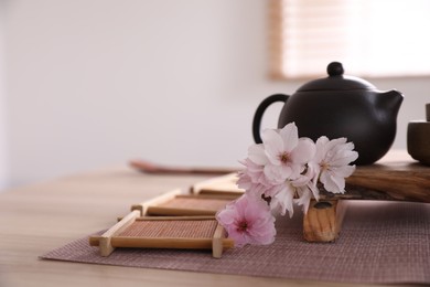 Pot, sakura flowers and bamboo coasters for traditional tea ceremony on table