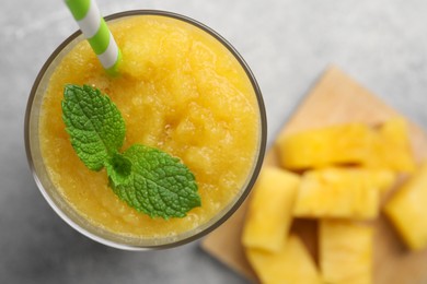 Photo of Glass of tasty pineapple smoothie with mint and cut fruit on light gray table, flat lay