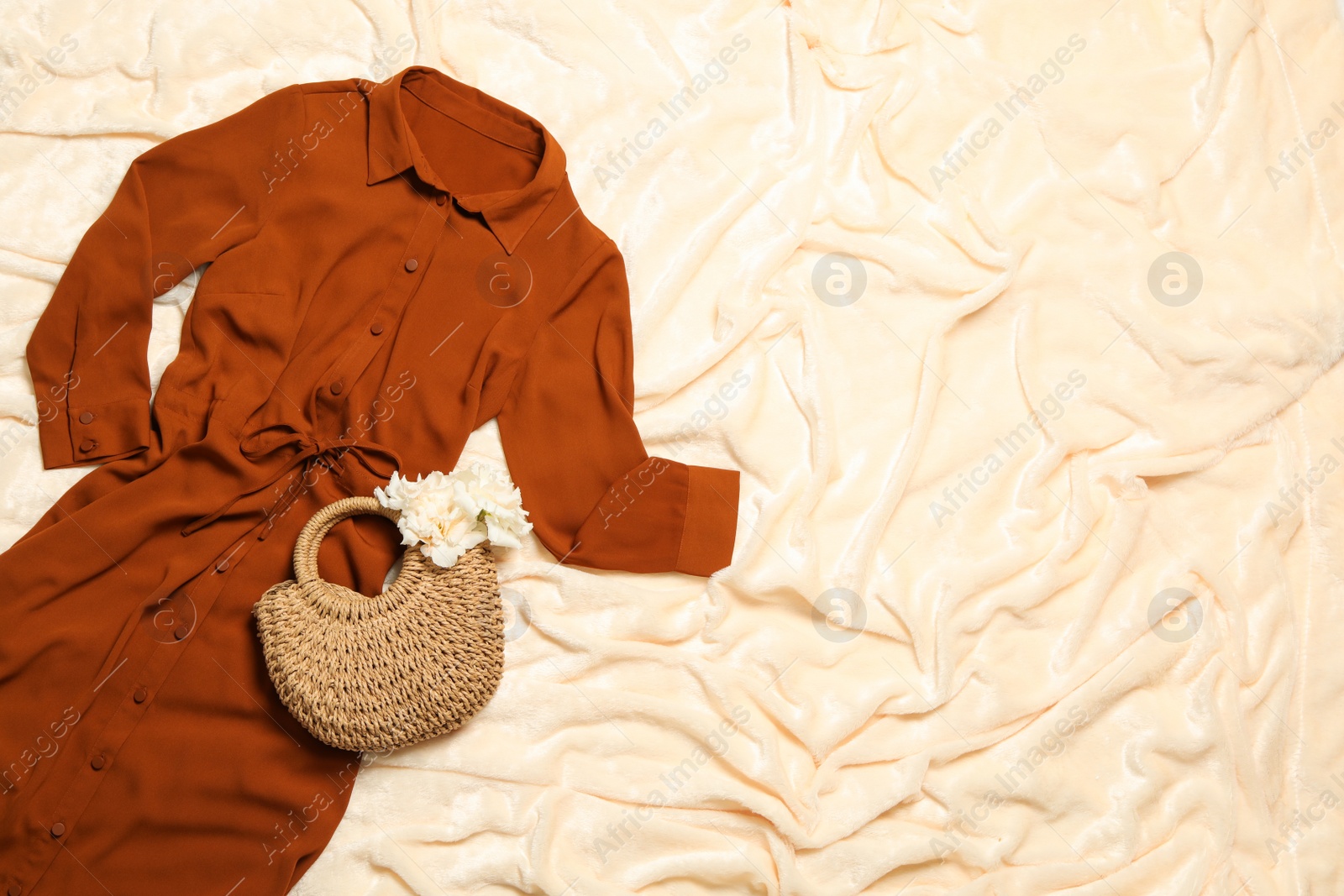Photo of Stylish brown dress and bag on beige blanket, flat lay. Space for text