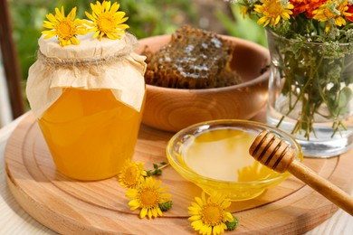 Photo of Delicious honey, combs and different flowers on wooden board in garden