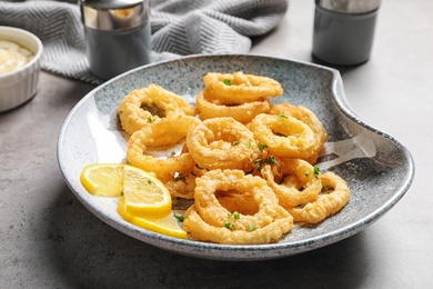 Plate with homemade crunchy fried onion rings and lemon slices on table