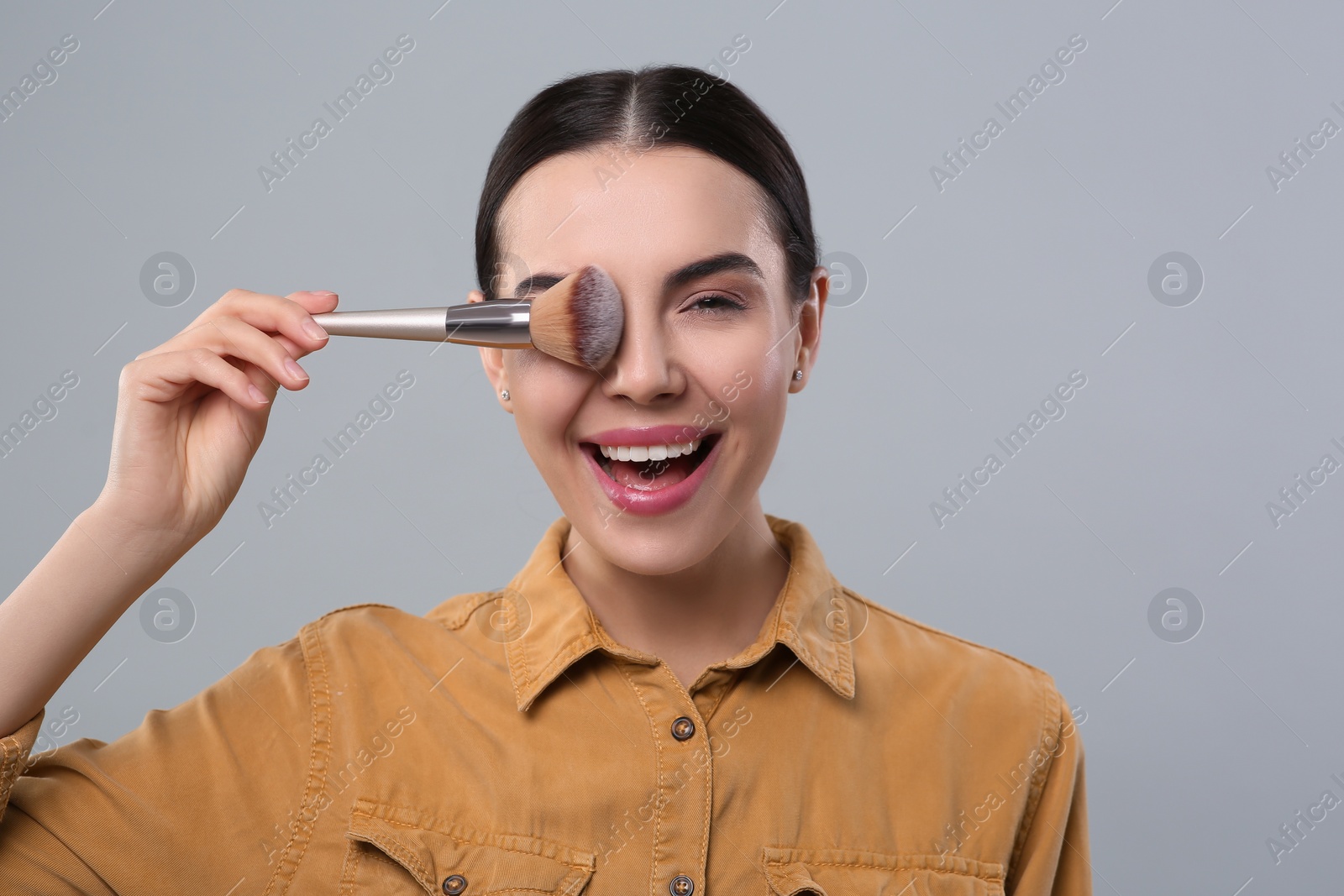 Photo of Happy woman with makeup brush on light grey background