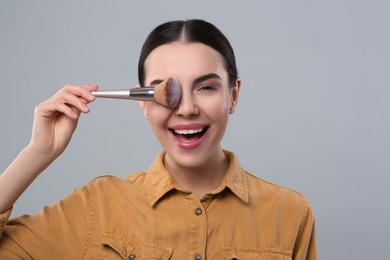 Happy woman with makeup brush on light grey background