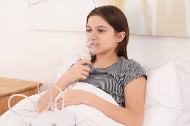 Photo of Cute girl using nebulizer for inhalation on bed at home