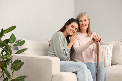 Photo of Mature lady with walking cane and young woman on sofa at home