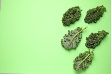 Photo of Fresh kale leaves on light green background, flat lay. Space for text