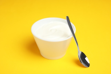 Photo of Bowl with creamy yogurt and spoon on color background