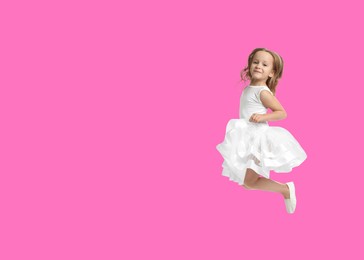 Cute girl jumping on bright pink background, space for text