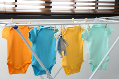 Different cute baby onesies hanging on clothes line indoors. Laundry day