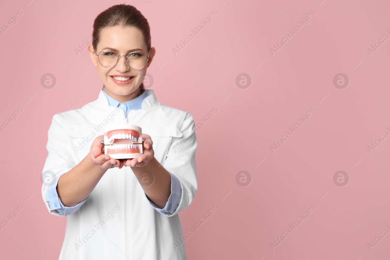 Photo of Female dentist holding jaws model on color background. Space for text